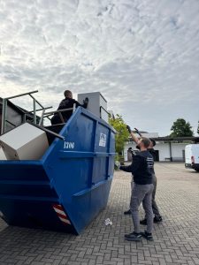 Zwei Personen bewegen große Möbelplatten neben einem blauen Container