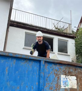 Person in Firmenkleidung mit Schutzhelm in einem blauen Container