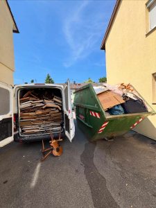 Mit Holzteilen beladener weißer Transporter neben einem grünen Container