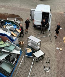 Vier Personen in Firmenkleidung neben einem Transporter und zwei blauen Containern