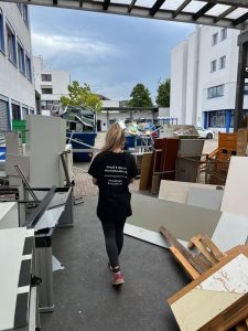 Person in Firmenkleidung neben bereitgestellten weißen Möbelteilen im Hof