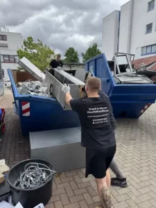 Eine Person trägt eine weiße Möbelplatte an einem blauen Container