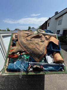 Grüner Container mit Teppichen, Säcken und Haushaltsgegenständen