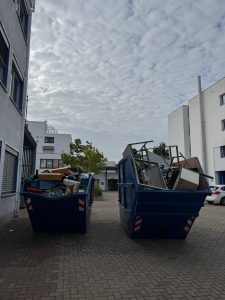 Zwei blaue Container mit Möbelteilen und Metallteilen im Hof