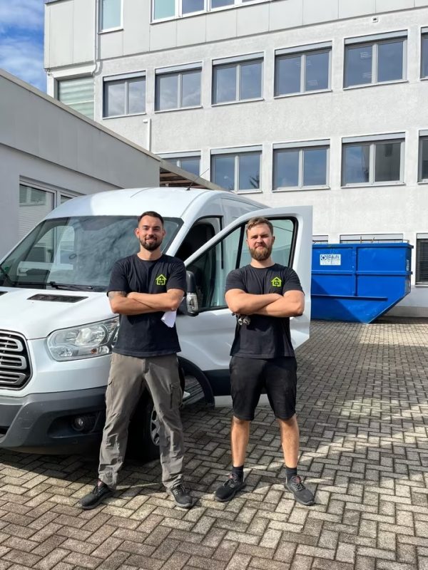Zwei Männer in Strauß-&-Werner-Kleidung vor einem weißen Transporter