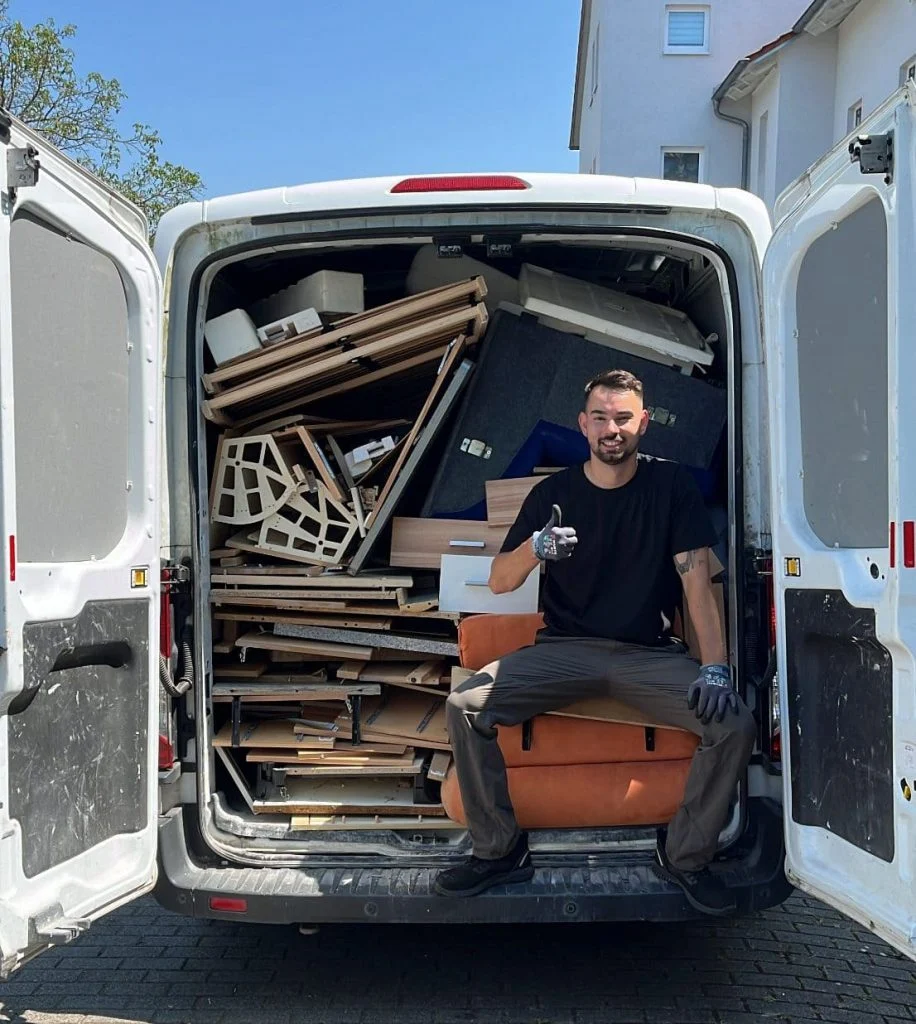 Ein Mann in Firmenkleidung am geöffneten Transporter mit abgebauten Möbelteilen